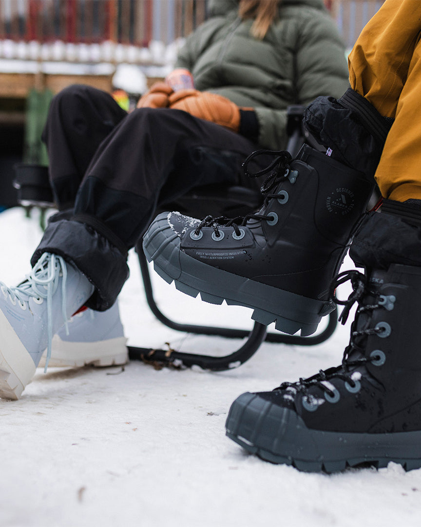 two people wearing boots and sitting in a chair. VBX LITE blue pair and black pair