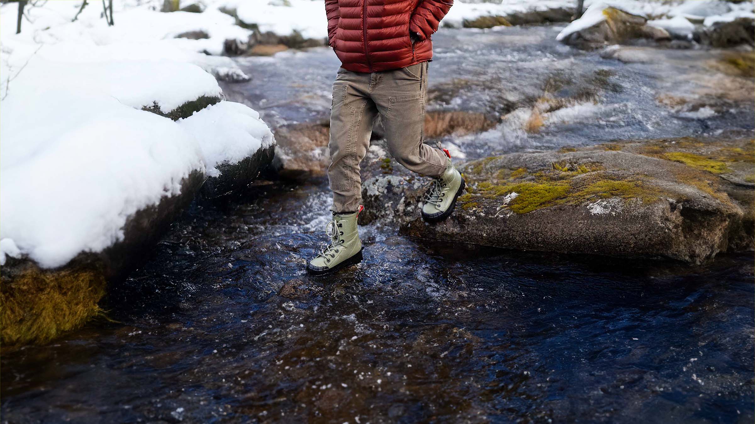 Person wearing waterproof snow boots walking through creek. 